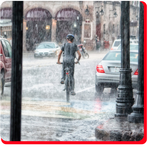 A cyclist rides through heavy rainfall in downtown Toronto, surrounded by vehicles and flooded streets—illustrating the severe impact of urban storms and the urgent need for commercial storm damage restoration services.