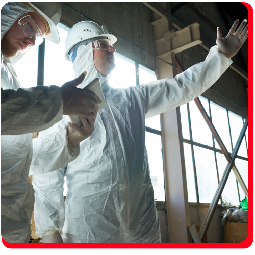 Two asbestos abatement professionals in full protective gear inspecting a commercial building in Toronto for hazardous material removal.