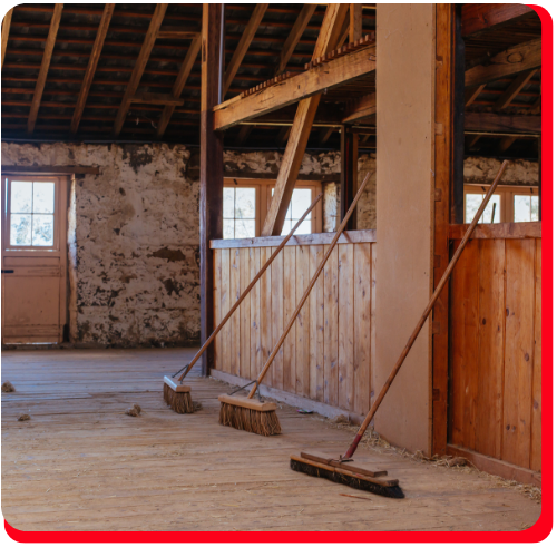An interior view of a historic barn in Toronto undergoing restoration, featuring wooden beams, stone walls, and brooms lined up for post-renovation cleanup.