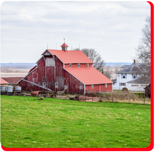 A large, weathered red barn with a pitched roof sits on a green field outside Toronto, representing a rural Ontario structure suitable for full barn restoration and preservation.
