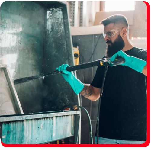 Technician in safety gear using a high-pressure hose to perform commercial mould removal on industrial surfaces.