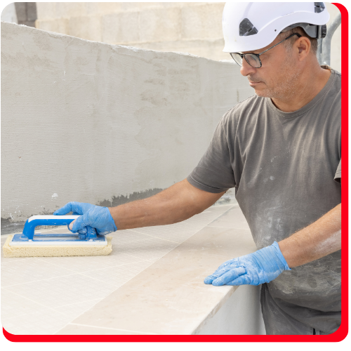 Construction worker in Toronto, Ontario, Canada wearing a hard hat and blue gloves, using a finishing tool to smooth a concrete surface during a building restoration project.
