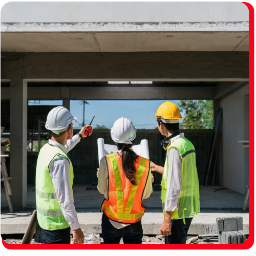 Team of construction professionals in Toronto, Ontario, Canada wearing safety helmets and reflective vests, reviewing blueprints and inspecting a concrete building during a restoration project.
