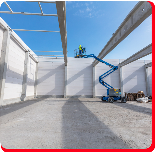 Construction worker in Toronto, Ontario, Canada operating a boom lift to perform concrete wall restoration inside a large industrial building under clear blue skies.