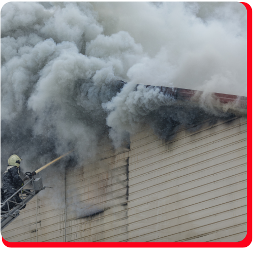 Firefighter on an aerial ladder spraying water into the roof of a commercial building engulfed in thick smoke—depicting emergency fire and soot cleanup for businesses. Firefighter on an aerial ladder spraying water into the roof of a commercial building engulfed in thick smoke—depicting emergency fire and soot cleanup for businesses.