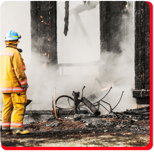 A firefighter stands in front of a smoke-filled, severely burned and collapsed structure, indicating the aftermath of a large-scale fire loss in Toronto, Ontario, Canada.