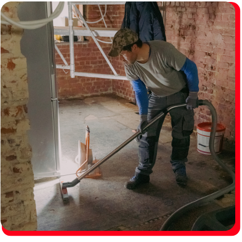 A commercial restoration technician uses a professional wet vacuum to extract standing water from a flooded brick-walled facility.