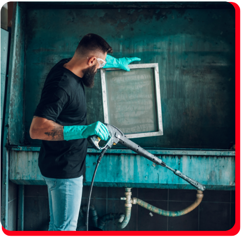 Bearded technician using pressure equipment to clean a mould-contaminated metal filter in a commercial setting.
