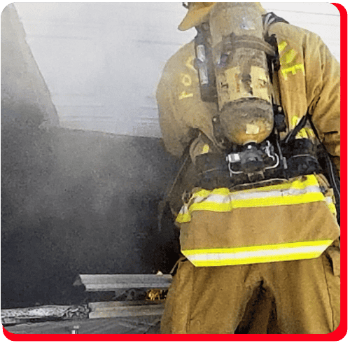 Firefighter in full gear responding to a smoke-filled commercial structure, with visible flames and smoke—representing commercial fire cleanup and smoke odor removal services.