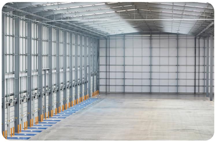 Spacious empty warehouse interior featuring a row of closed loading dock doors on the left, blue dock levelers, a high ceiling, and polished concrete floors. Bright, even lighting enhances the open area—perfect for businesses in need of commercial restoration services such as commercial fire restoration or commercial water damage restoration after fire damage or flooding.