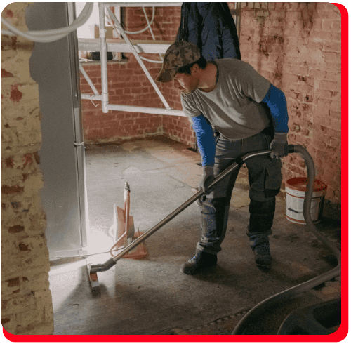 A commercial restoration technician uses a professional wet vacuum to extract standing water from a flooded brick-walled facility.