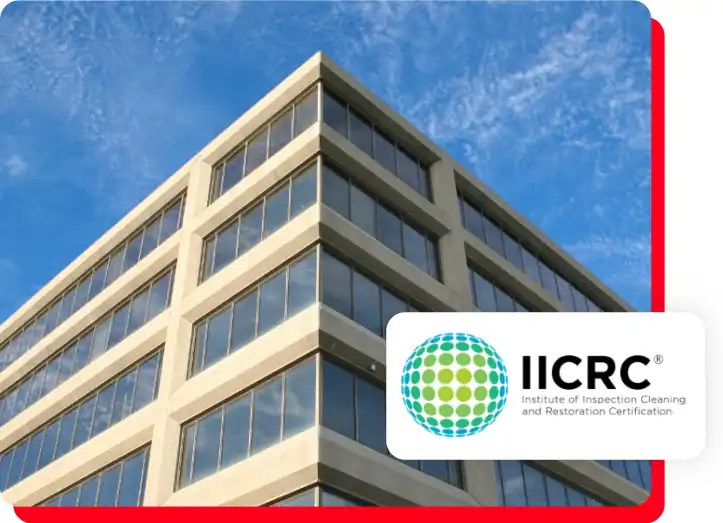 A modern office building under a blue sky features the IICRC (Institute of Inspection Cleaning and Restoration Certification) logo prominently in the foreground, showcasing expertise in commercial restoration services such as water damage restoration, fire damage restoration, commercial fire restoration, and especially commercial water damage restoration.