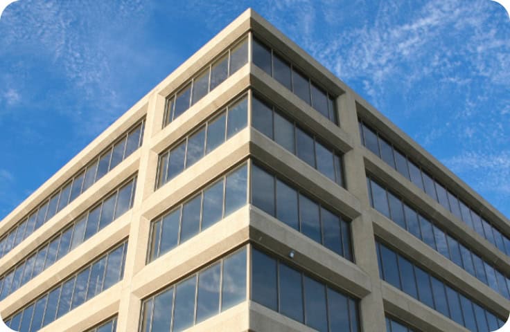A modern office building with large glass windows on each floor stands against a bright blue sky with wispy clouds, emphasizing the crucial role of commercial restoration, fire damage restoration, water damage restoration, and specialized commercial fire and water damage restoration services in preserving its impressive appearance.