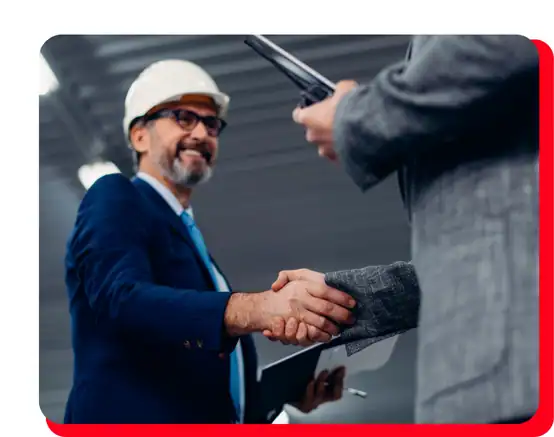 A man in a hard hat and suit smiles while shaking hands with another person in a business suit, symbolizing a successful partnership or agreement in an industrial environment focused on commercial restoration services such as water damage restoration, fire damage restoration, commercial fire restoration, and commercial water damage restoration.