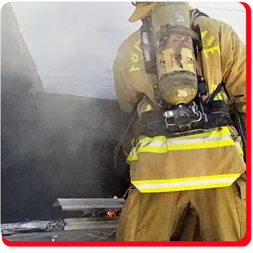 A firefighter in full gear stands near smoke and small flames, facing away from the camera and responding to a commercial fire restoration emergency, illustrating the crucial first steps of fire damage restoration and water damage restoration services essential for commercial buildings.