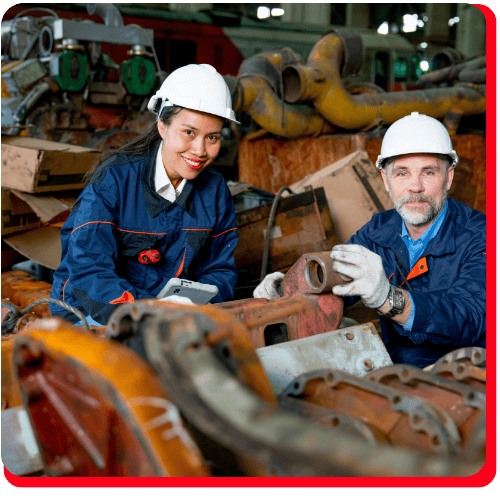 Two engineers in safety helmets and overalls collaborate in an industrial environment, inspecting machinery parts and smiling at the camera. The area features mechanical equipment and rusted metal components, highlighting the intricate steps of commercial restoration processes such as fire damage restoration, water damage restoration, commercial fire restoration, and commercial water damage restoration.