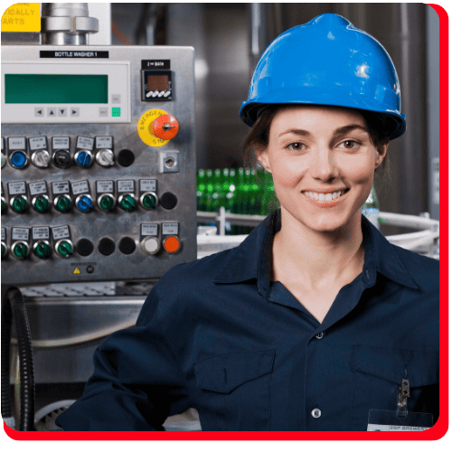 A woman wearing a blue hard hat and navy work shirt stands smiling before industrial control panels, with green bottles in the background, indicating a factory or bottling plant—an environment where commercial restoration services such as fire damage restoration, water damage restoration, commercial fire restoration, or commercial water damage restoration may be critical.