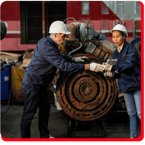 Two workers in hard hats and gloves inspect a large, rusted mechanical engine part in an industrial setting, appearing to assess it for commercial restoration after fire or water damage. One worker hands a tool to the other, suggesting active efforts toward commercial fire restoration or commercial water damage restoration.