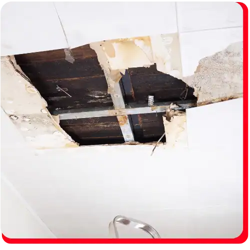 A section of ceiling shows significant damage, with plaster missing and both wooden beams and metal supports exposed—common indicators of commercial restoration needs. The stained, crumbling area around the hole suggests fire damage restoration or water damage restoration may be required. Part of a metal ladder is visible at the bottom, indicating ongoing commercial fire restoration or commercial water damage restoration work.