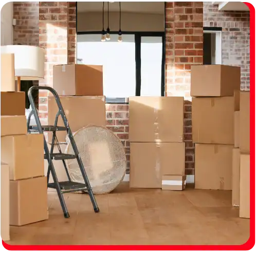 A stack of cardboard moving boxes, a metal ladder, a floor lamp, and a fan are in a room with brick walls and wooden floors—typical equipment seen during commercial restoration projects such as commercial water damage restoration or fire damage restoration.